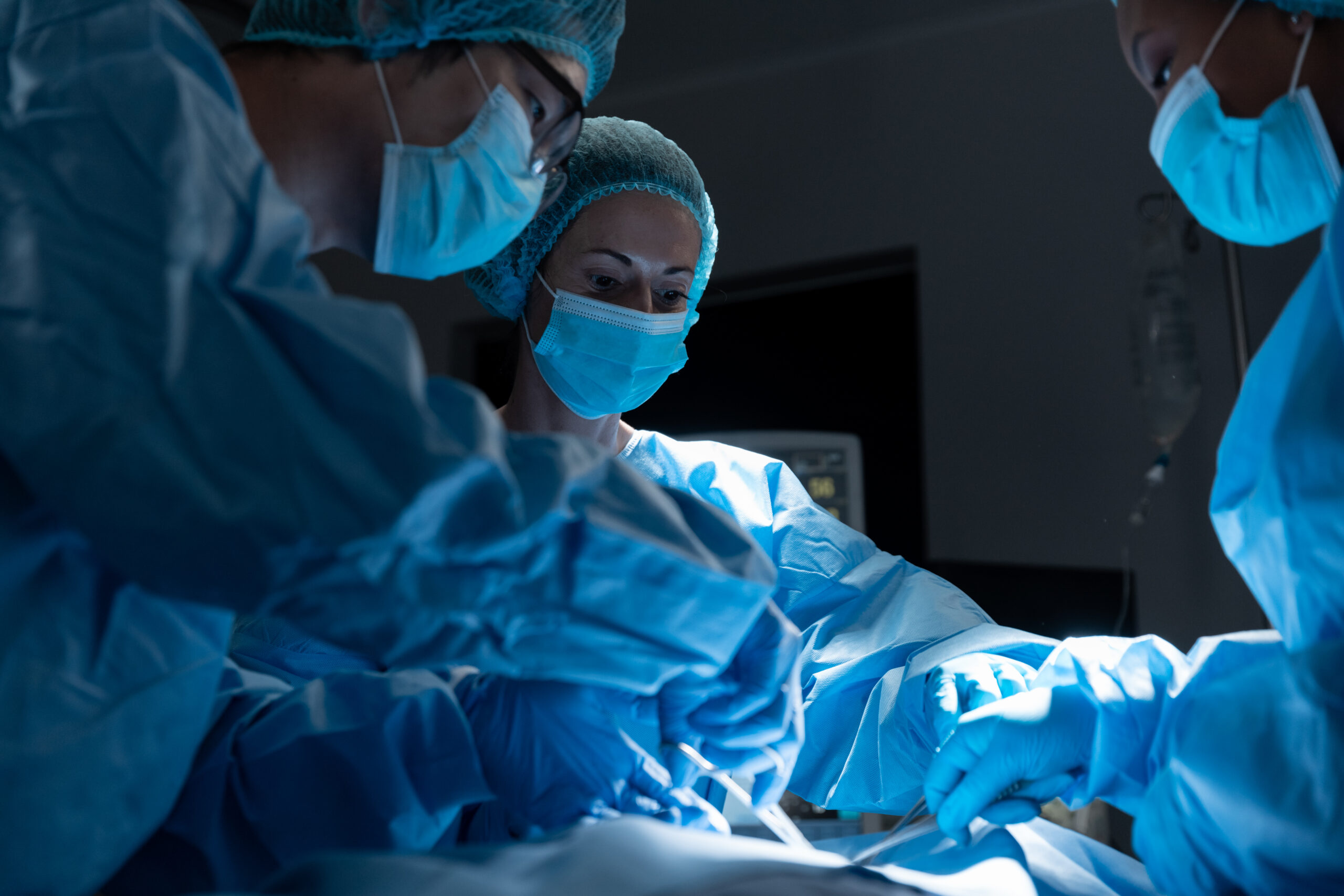 Diverse group of male and female surgeons in operating theatre wearing face masks performing surgery. medicine, health and healthcare services during coronavirus covid 19 pandemic.