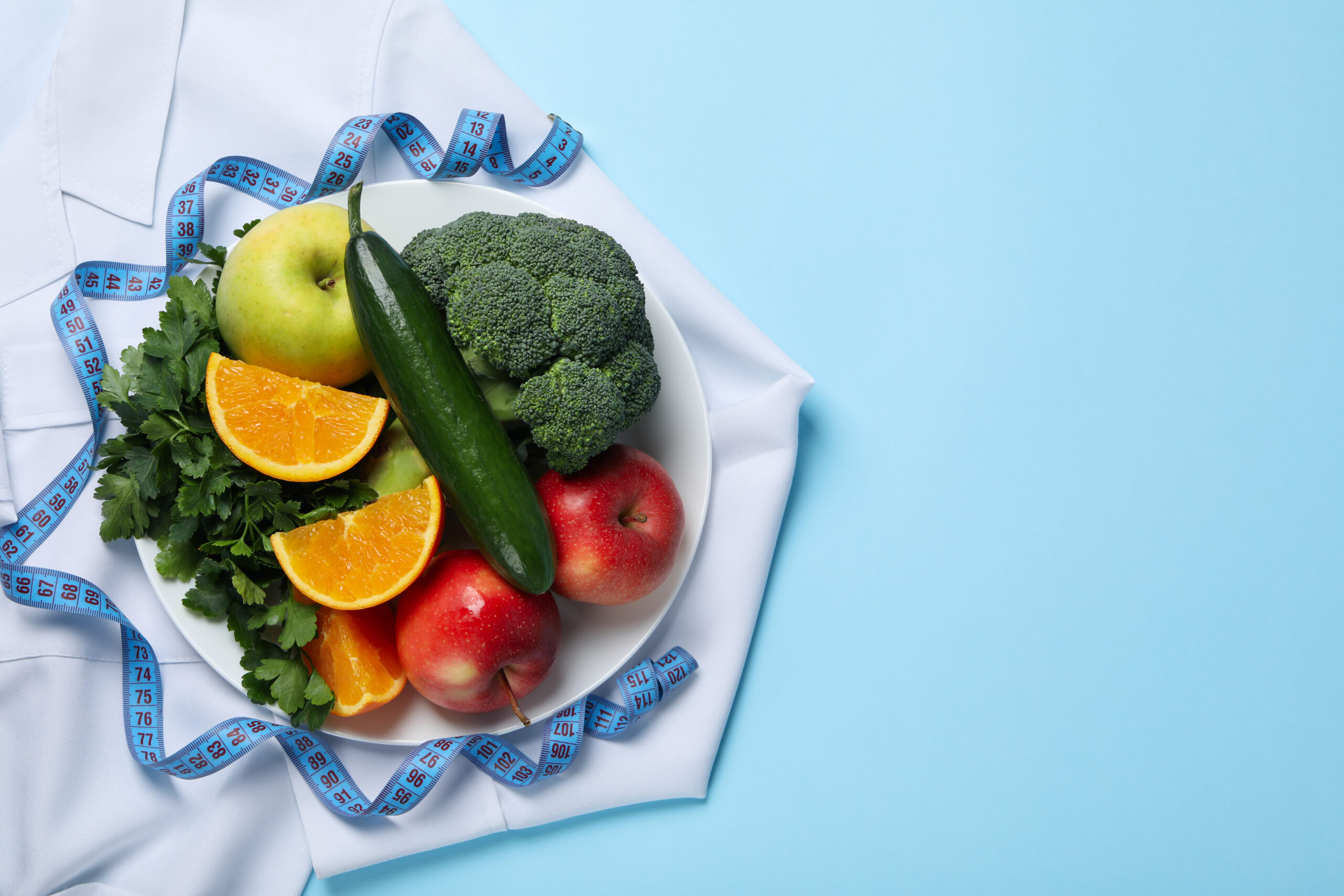 Doctors coat, healthy food and measuring tape on blue background - weight loss